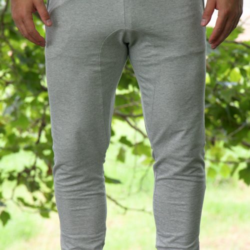 A person wearing Genesis Joggers - Grey with adjustable fit and zipper pockets, paired with white sneakers, stands on grass with green trees in the background. Their upper body is mostly out of frame.