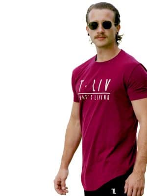 A man with long hair, a mustache, and sunglasses wears the Genesis Tee - Maroon featuring "T. LIV WHAT'S LIVING" text. He stands against a white background, looking slightly to the left.