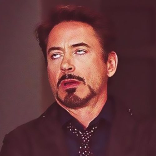 A man with short dark hair and a goatee is wearing a suit and patterned tie. He is rolling his eyes upward with an exasperated expression, conveying annoyance or disbelief. The background is dark and blurred.