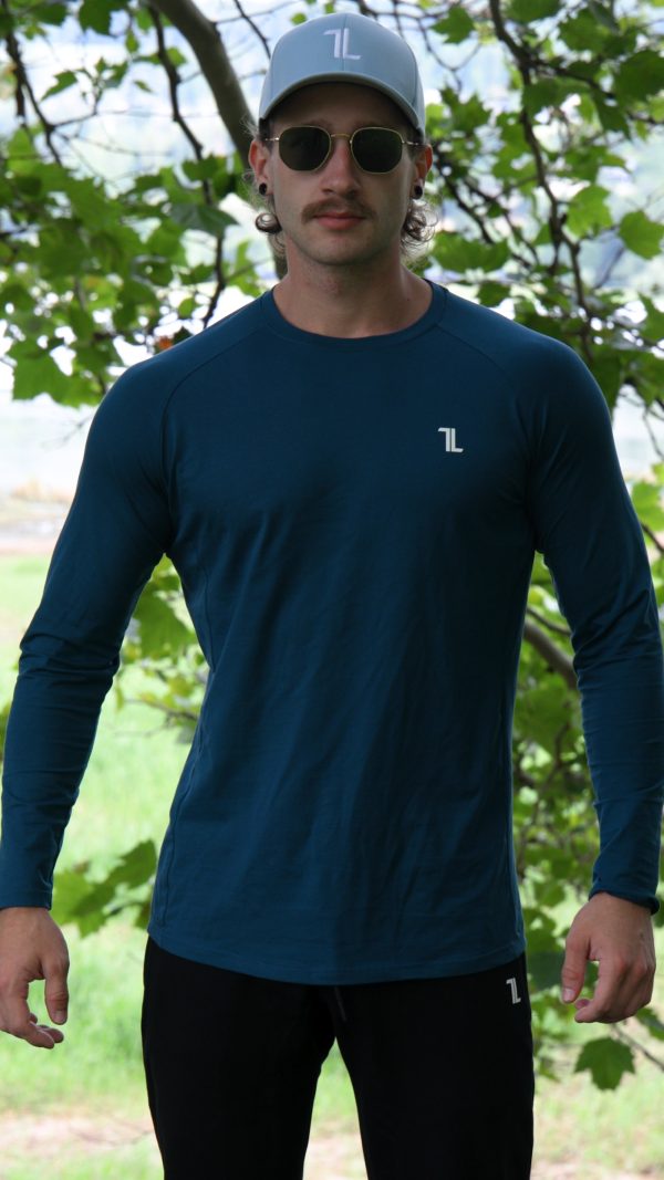 A man outdoors in front of leafy green trees, wearing sunglasses, a light blue cap, and the FRMR Long sleeve - Deep Ops gym shirt, looks at the camera.