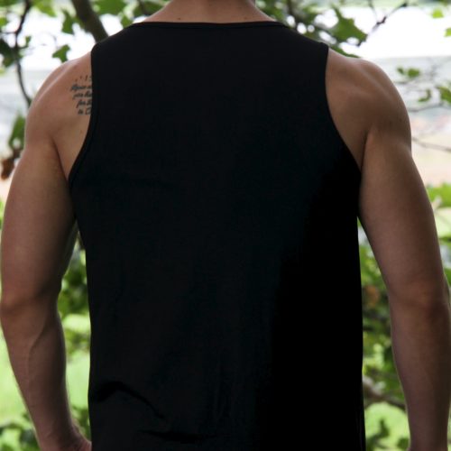 A person with medium-length hair stands outdoors facing away, wearing the Genesis Tank V2 - Black. The minimalist men’s performance tank features a TL logo and reveals part of a tattoo on their upper left shoulder amid greenery.