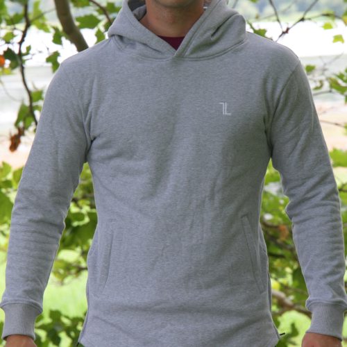 A man wearing the SPEKTR Hoodie - InfraGrey and sunglasses stands outdoors in front of leafy green trees, with blurred grass and sky in the background.