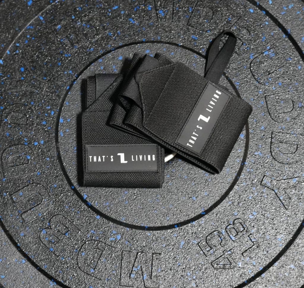 A pair of Copy of IronHide Lifting Straps labeled "THAT'S L LIVING" rests on a black, speckled 55 lb weight plate with indented lettering.