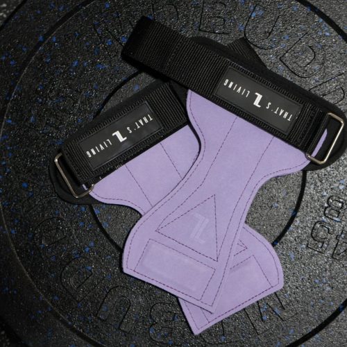 A pair of IronHide Lifting Straps – Black with white branding rests on a black 45-pound rubber-coated weight plate. The background is a speckled gym floor.