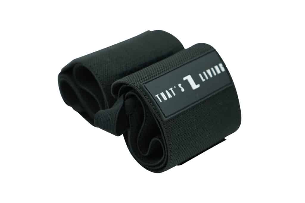 A pair of Original Wrist Wraps in black fabric, rolled up with a rectangular label displaying "That's Living" in white on a black background.