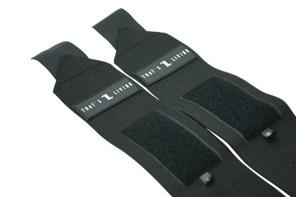 Close-up of two Original Wrist Wraps, black with Velcro sections and label tags reading "THAT'S LIVING" in white text, laid side by side on a white background.