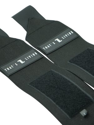Close-up of two Original Wrist Wraps, black with Velcro sections and label tags reading "THAT'S LIVING" in white text, laid side by side on a white background.