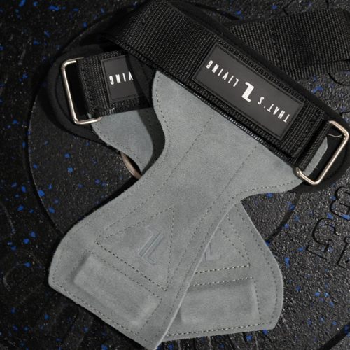 A pair of IronHide Lifting Straps with gray suede grips, black straps, and metal loops rest crossed on a black 45 lb weight plate with blue specks.