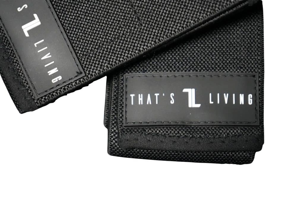 Two black Original Elbow Wraps with textured fabric surfaces, each featuring a label that reads "THAT'S L LIVING" in white text on a black background. The wraps are shown folded and partially stacked.