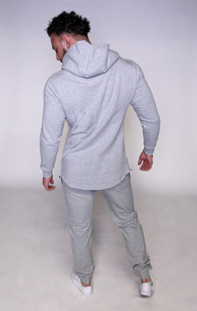 A man wearing the SPEKTR Hoodie in light gray, along with matching sweatpants and white sneakers, stands with his back to the camera on a plain light background.