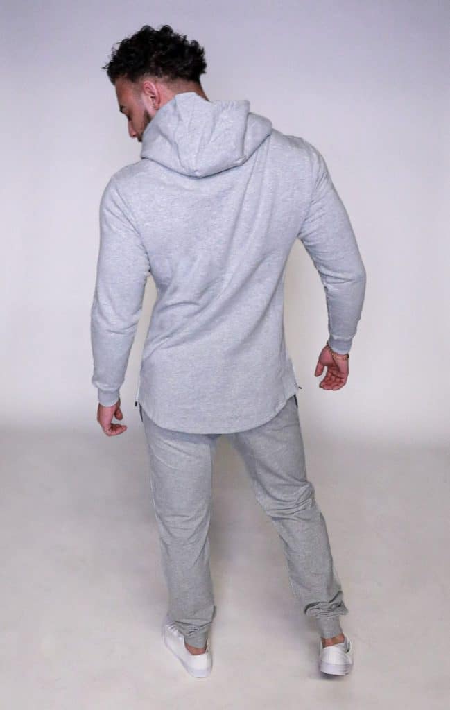 A man wearing the SPEKTR Hoodie in light gray, along with matching sweatpants and white sneakers, stands with his back to the camera on a plain light background.