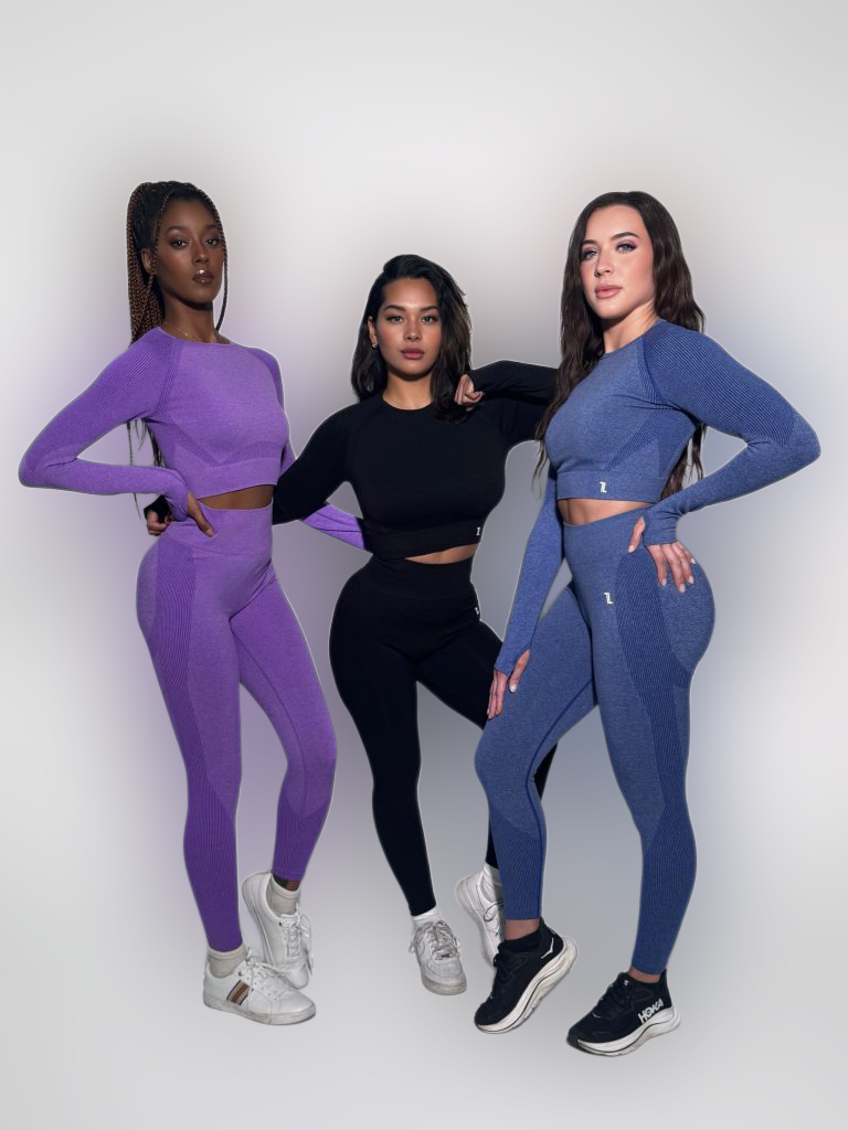Three women pose confidently in Allure Set V2 activewear—matching long-sleeve crop tops and high-waisted leggings in purple, black, and blue—standing against a plain white background.