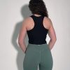 A person with curly hair faces away from the camera, wearing the LuxeForm Tank in black and green leggings, hands resting behind their back against a plain backdrop.