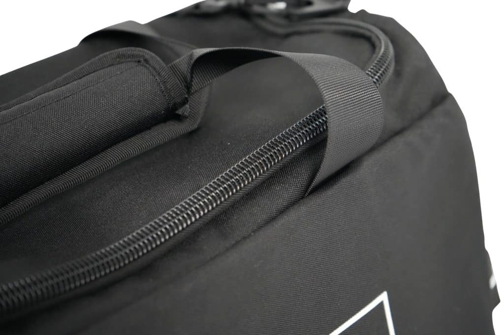 Close-up of the TRIARC Duffle Bag in black fabric, featuring a padded handle, partially visible zipper, and a top strap. The white background accentuates the bag's texture and detailed design.