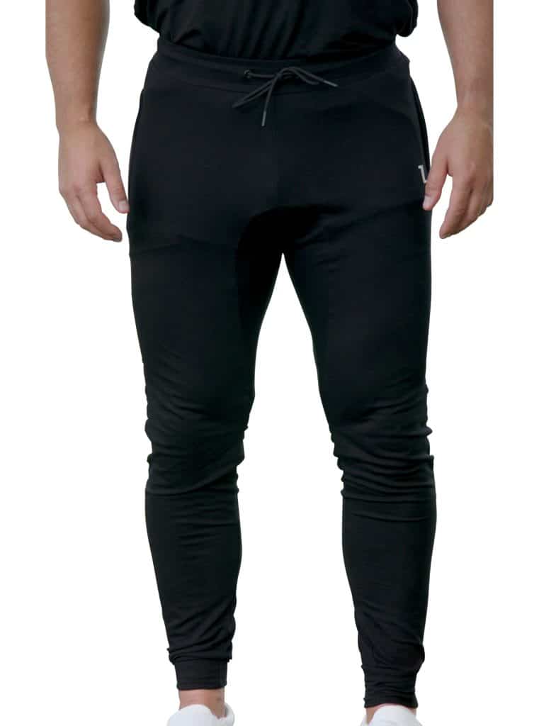 A person wearing fitted black jogger pants with a drawstring waist, standing upright. Only the lower half of the body is visible, showing white shoes and hands relaxed at the sides.