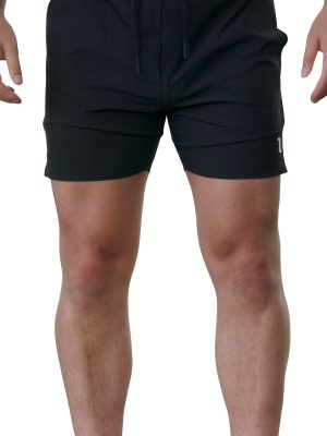 A person wearing black athletic shorts with a small white logo on the left leg stands against a white background; only the lower torso and legs are visible.