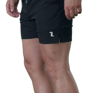 A person wearing black athletic shorts with a small white logo on the left leg stands against a white background; only the lower torso and legs are visible.