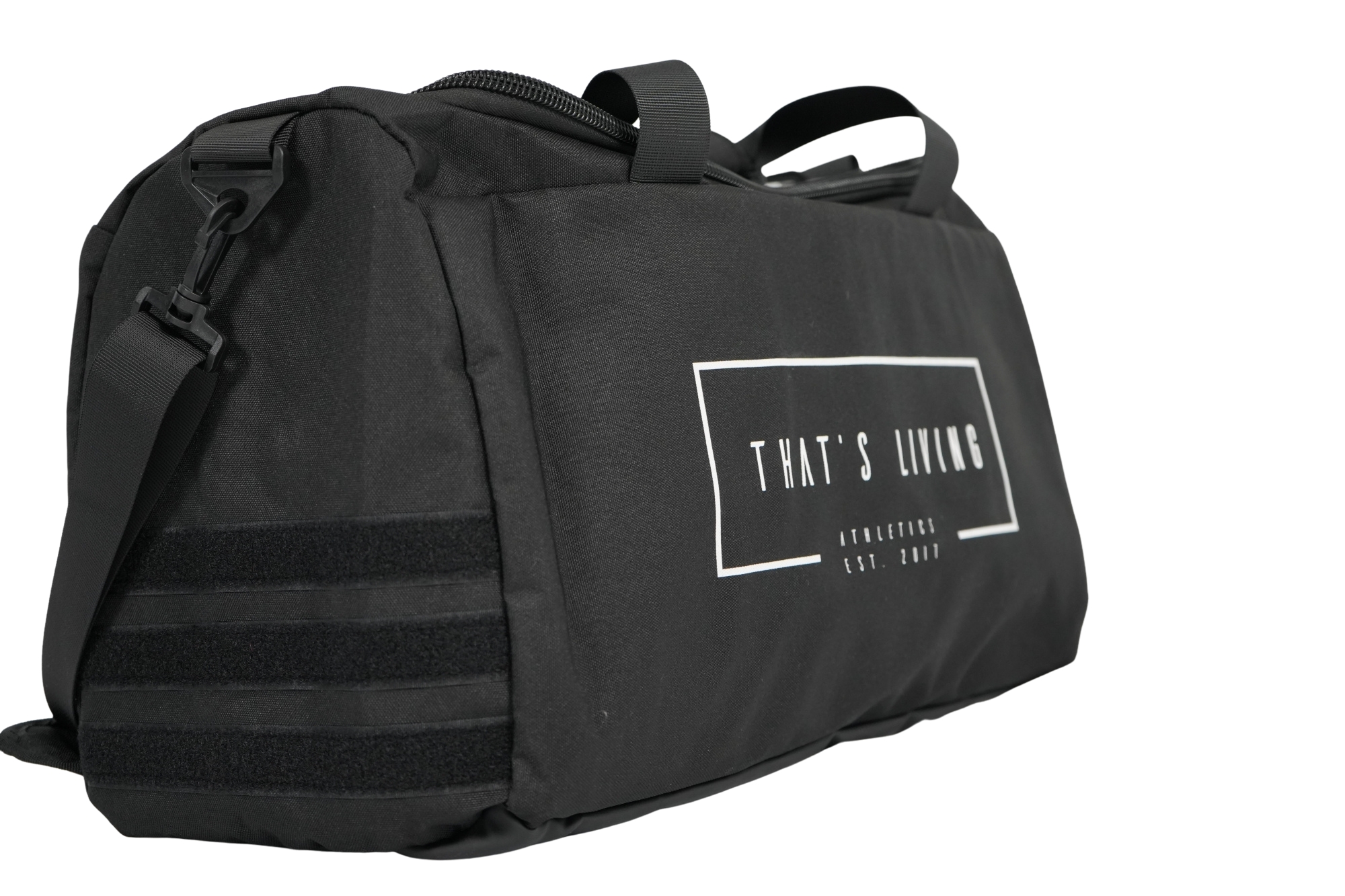 The TRIARC Duffle Bag is black with a shoulder strap, a zippered top, and features subtle horizontal stripes on one end. A rectangular side logo displays "THAT'S LIVING" in white text.