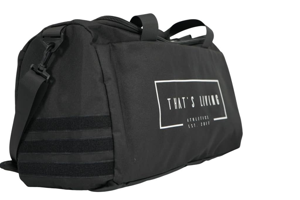 The TRIARC Duffle Bag is black with handles and a shoulder strap. It features a rectangular white "THAT'S LIVING" logo with smaller text beneath it on one side.