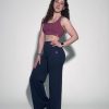 A woman with long curly hair wears a mauve sports bra, high-waisted navy blue wide-leg pants, and white sneakers, standing against a plain light background and posing with one hand on her hip.