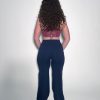 A person with long curly hair stands facing away, wearing a maroon crop top and black high-waisted pants, against a plain white background.