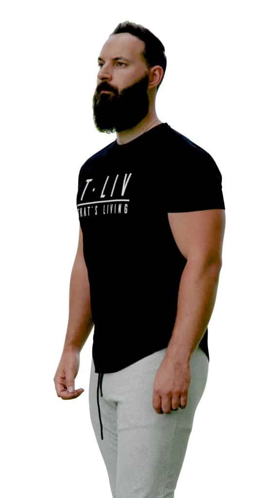 A man with a full beard stands facing left, wearing a black T-shirt with white text and light gray sweatpants, against a white background.