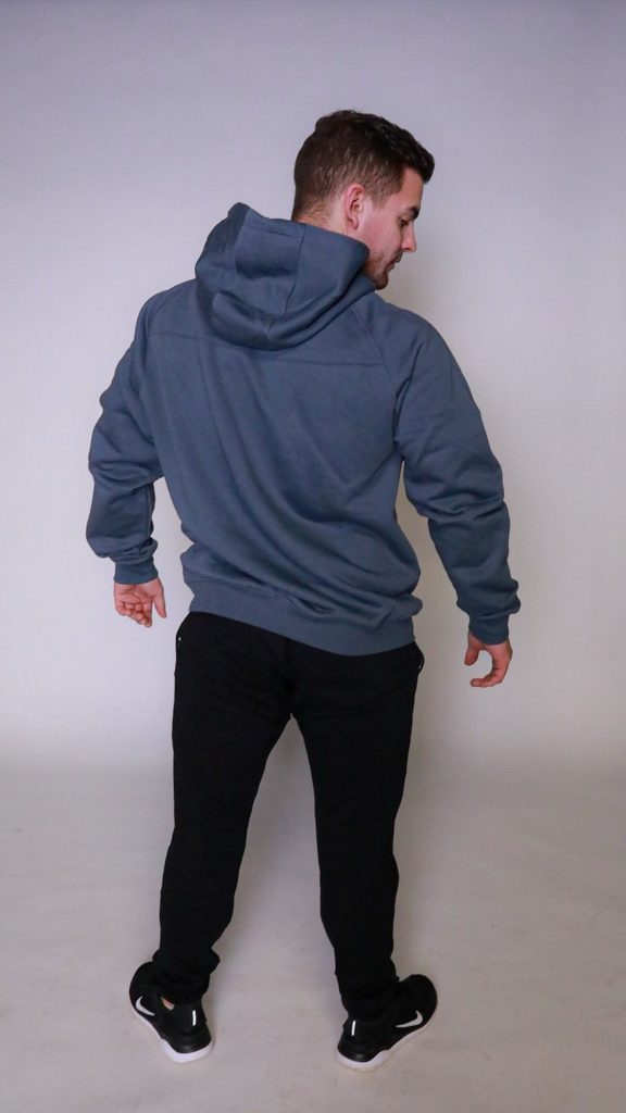 A man faces away from the camera, wearing the FORGE HOODIE with a tapered fit and scoop bottom, black pants, and black sneakers, set against a plain light background.
