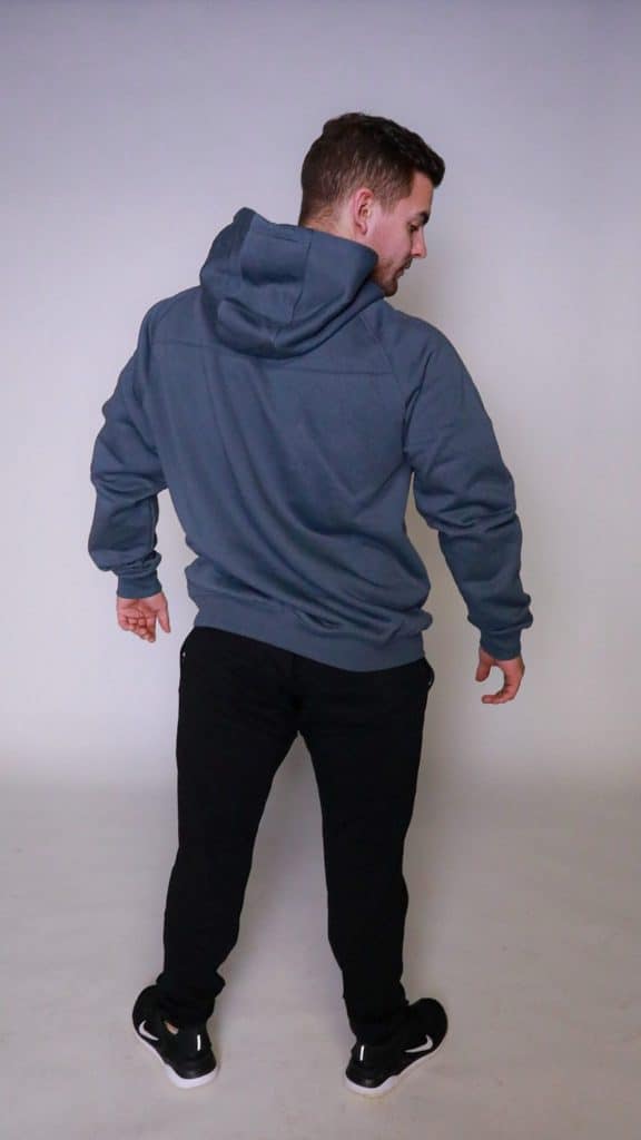 A man faces away from the camera, wearing the FORGE HOODIE with a tapered fit and scoop bottom, black pants, and black sneakers, set against a plain light background.