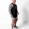 A muscular man with a large arm tattoo wears a black tank top, light green shorts, and sneakers, standing confidently against a plain white background.