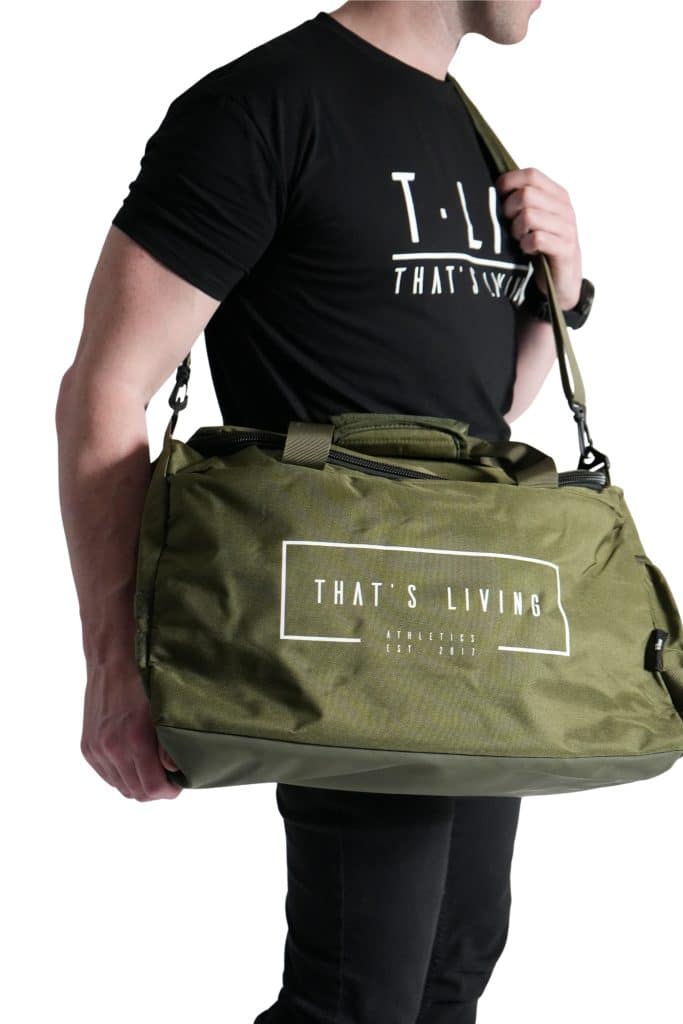 A person in a black "That's Living" t-shirt holds an olive green TRIARC Duffle Bag, both featuring the same logo and text, against a white background. The image is cropped to show only the body from the neck down.