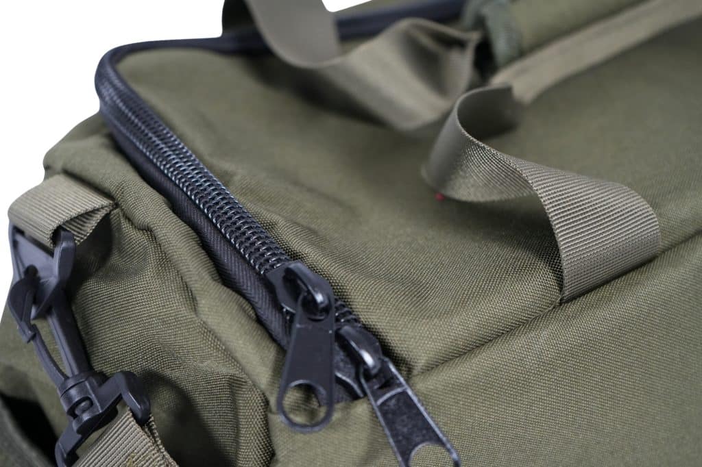 Close-up of the TRIARC Duffle Bag in olive green, featuring a black zipper, beige webbing straps, and a plastic buckle. The image highlights the fabric texture and detailed construction of the bag.