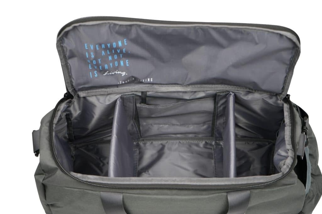 The TRIARC Duffle Bag is an open gray bag with multiple interior compartments and the printed text “Everyone is alive, but not everyone is living” on the inside flap.