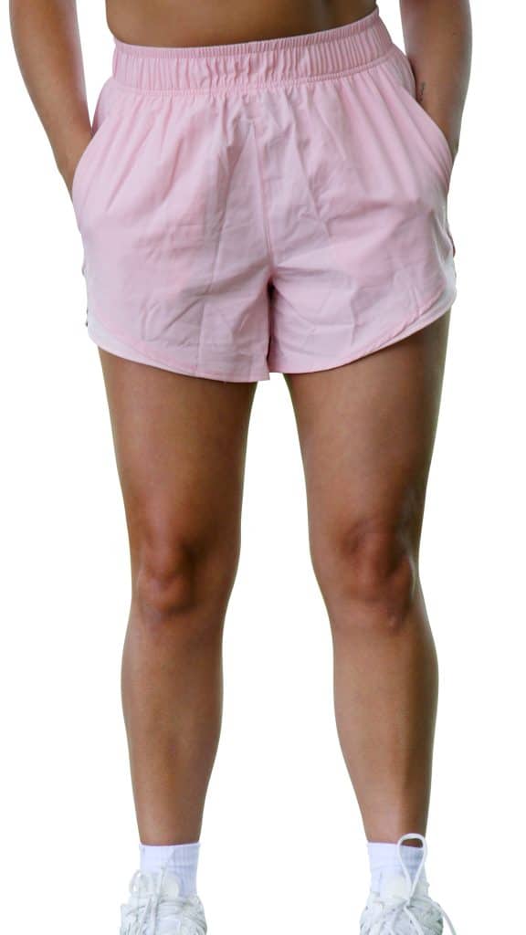 Person standing with hands in pockets, wearing light pink shorts and white sneakers. The image is cropped from the waist down, isolated on a white background.