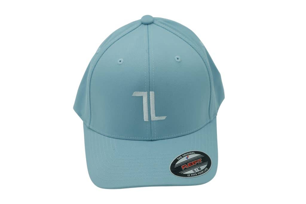 A light blue baseball cap with a white stylized "TL" logo on the front, viewed from the front. There is a black and red Flexfit sticker on the brim.