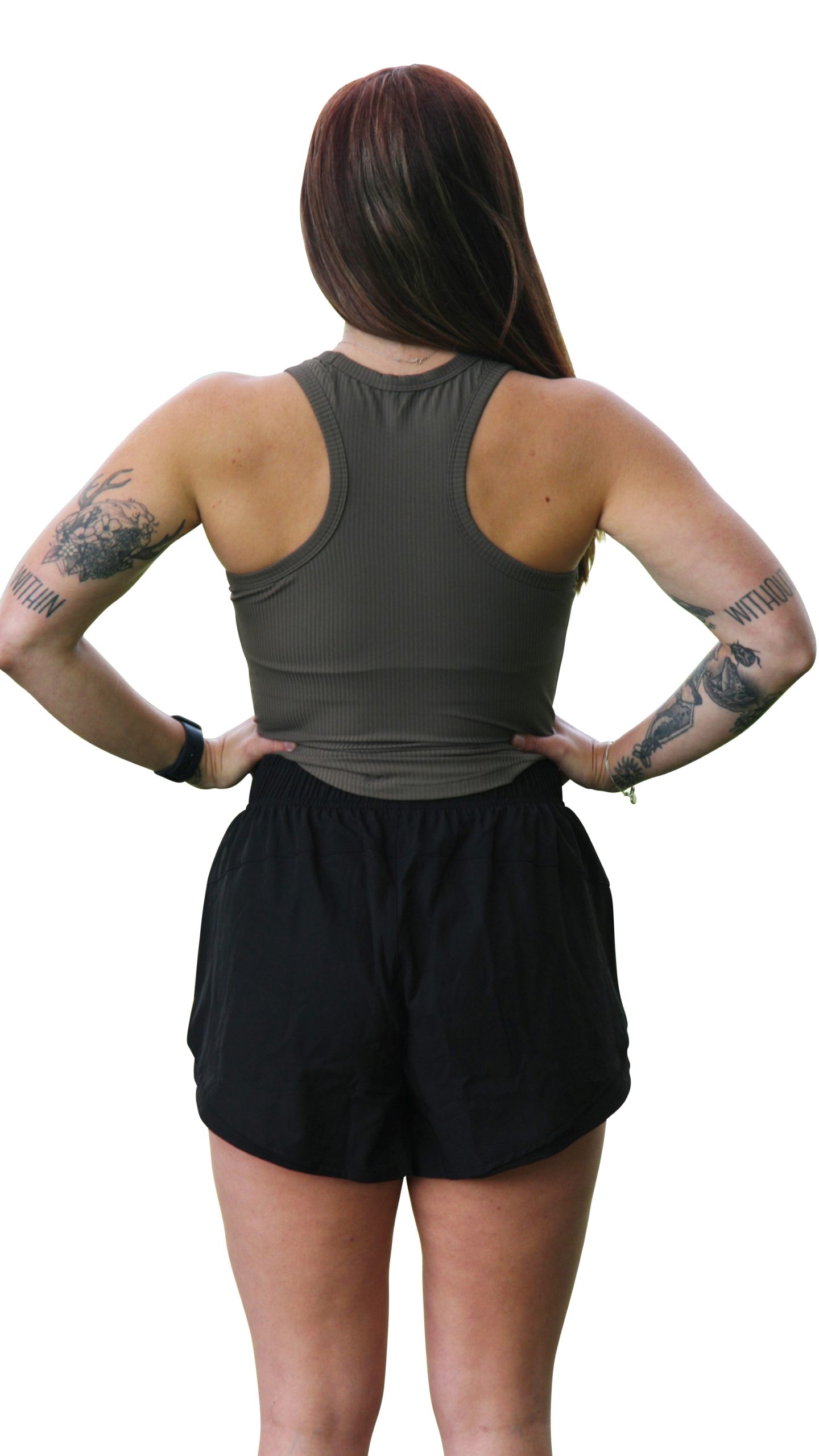 A woman with long hair stands with hands on hips, facing away from the camera in a sleeveless dark green ribbed top and GLYDE Shorts. Tattoos are visible on both arms against a white background.