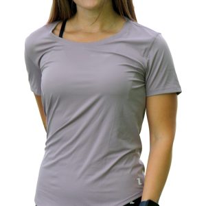 A woman with long brown hair wearing a light purple short-sleeve shirt, black leggings, and a smartwatch stands facing forward with a neutral expression against a white background.