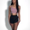 Pink 5 A woman stands against a plain white background, wearing a light purple crop top and black athletic shorts. She has long dark hair and poses with her hands resting on her thighs, looking confidently at the camera.