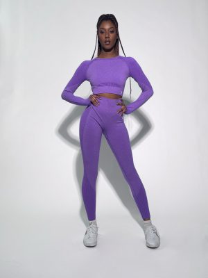 A woman wearing a light green, long-sleeve crop top and matching leggings poses standing sideways. She is wearing maroon athletic shoes and is set against a plain white background.