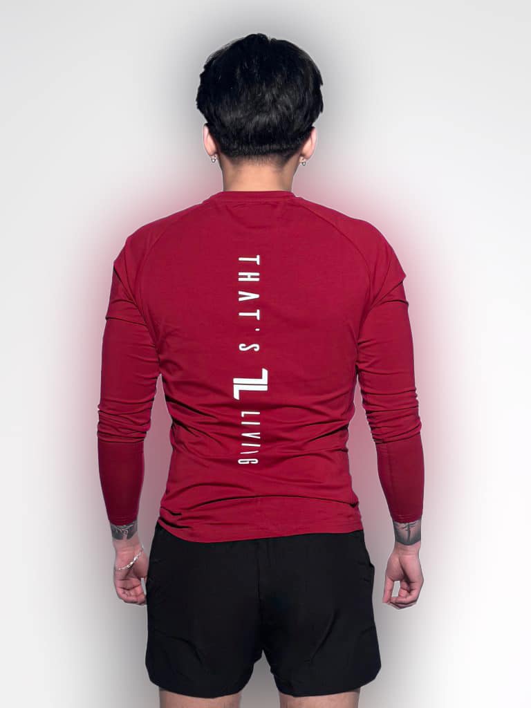 A person wearing a long-sleeve red shirt with the text "THAT'S LIVING" printed vertically on the back stands facing away, also wearing black shorts against a plain white background.