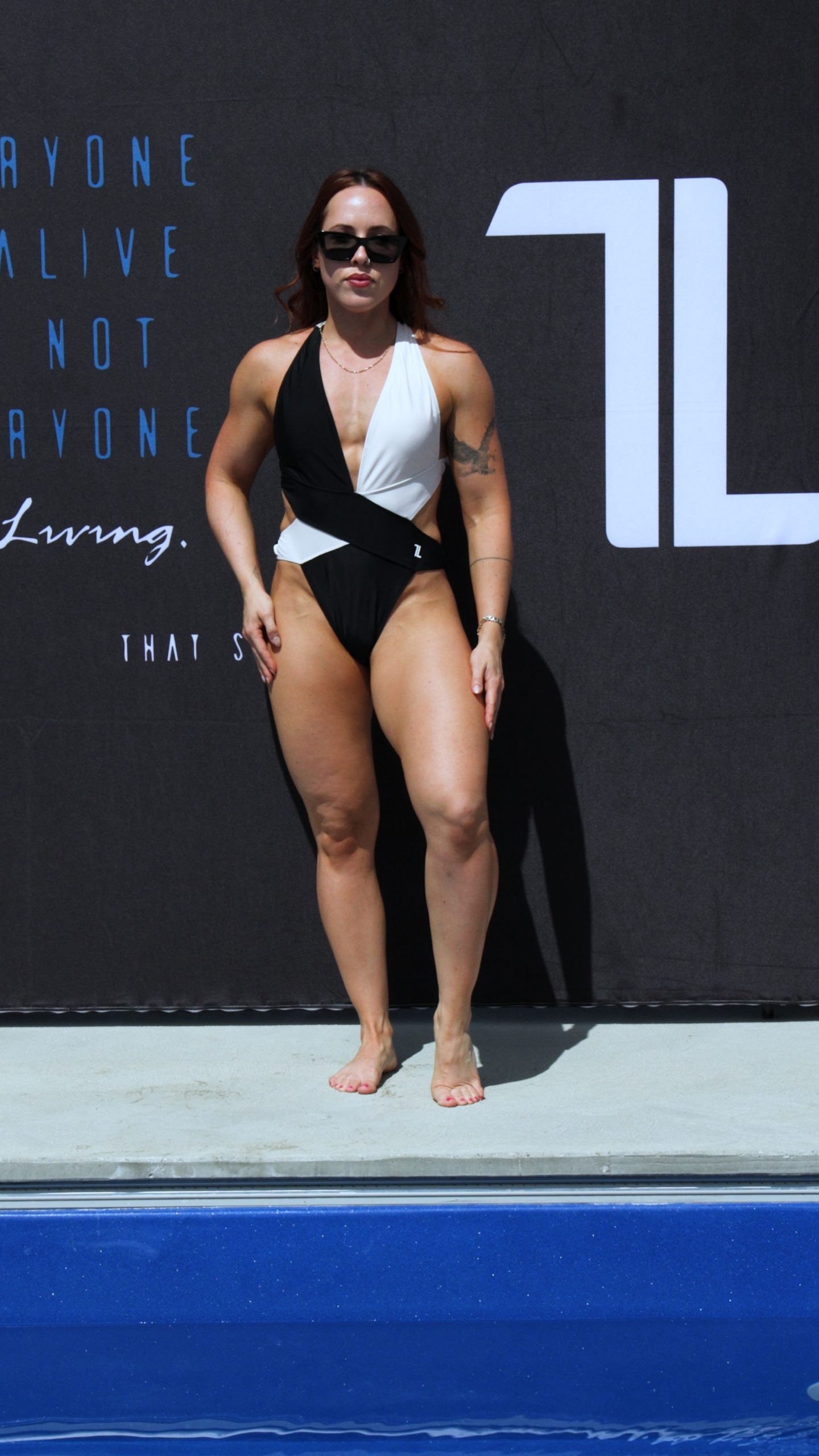 A woman wearing a black and white swimsuit and sunglasses stands poolside in front of a dark backdrop with white and blue text.